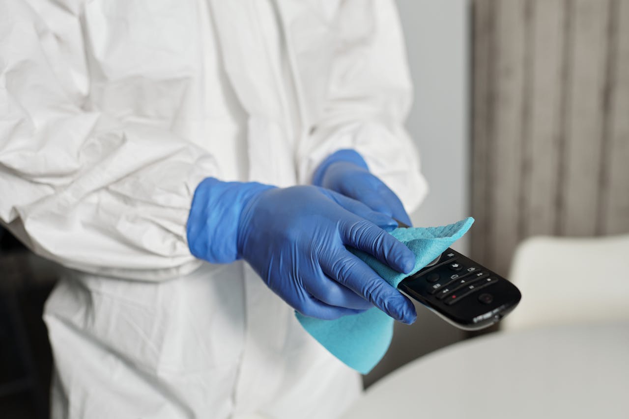 why-choose-us Close-up of a person disinfecting a remote control wearing protective gloves, ensuring cleanliness.