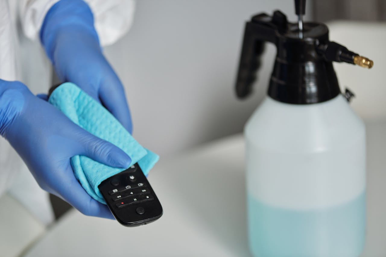 about-01 Close-up of gloved hands disinfecting a remote control with a cloth and spray bottle.